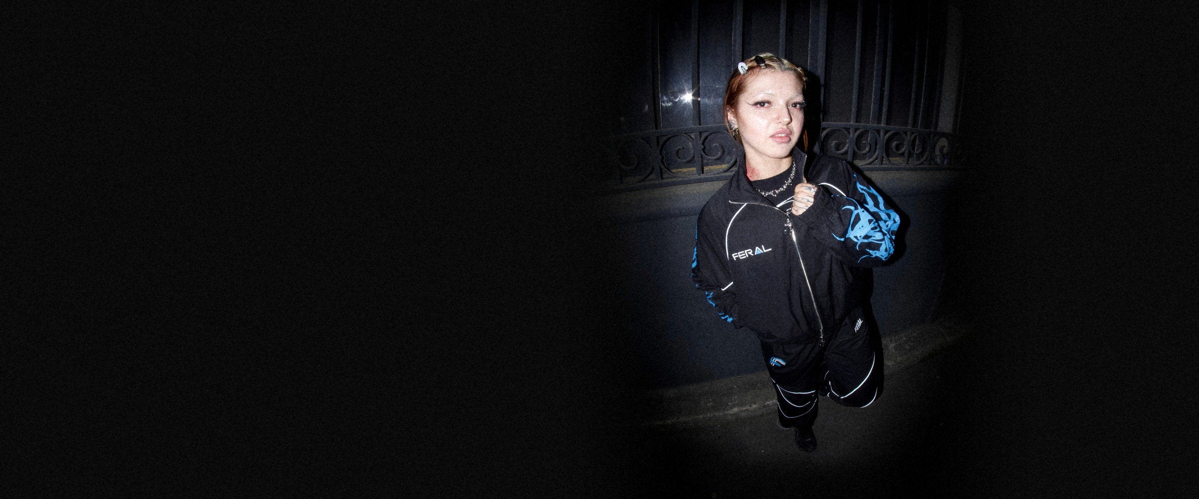 The FERAL Tribal Racer windbreaker set, black with blue tribal sleeves and white piping, worn at night