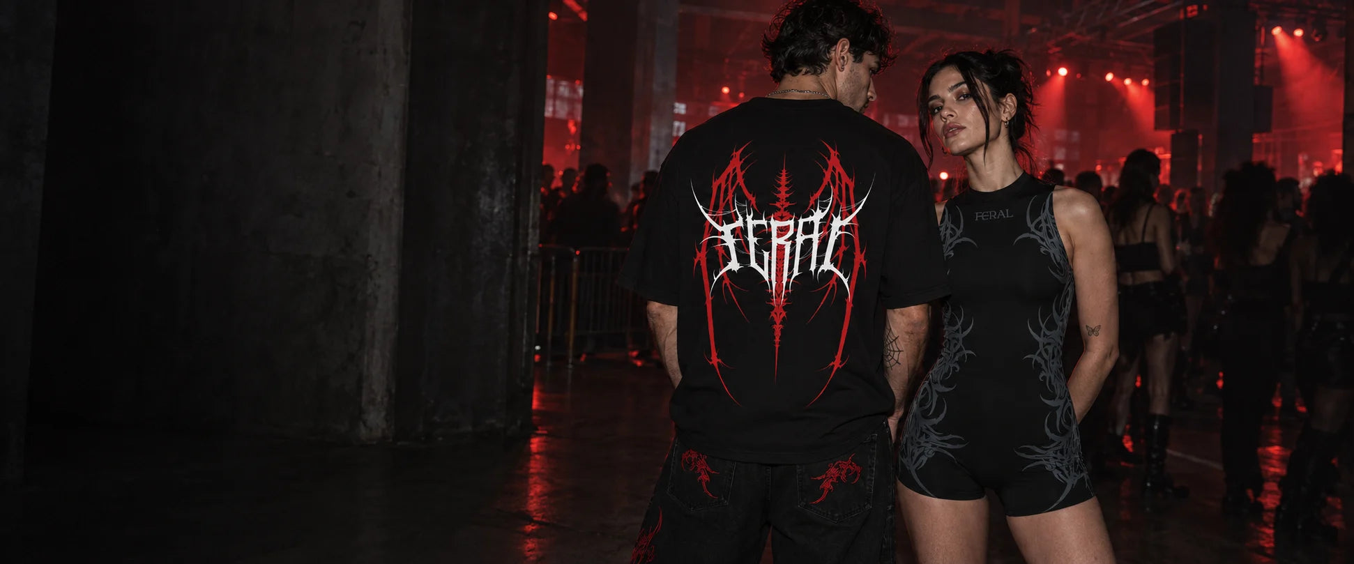 FERAL Barbed Dominion graphic tee and black sigilism romper in a warehouse club scene
